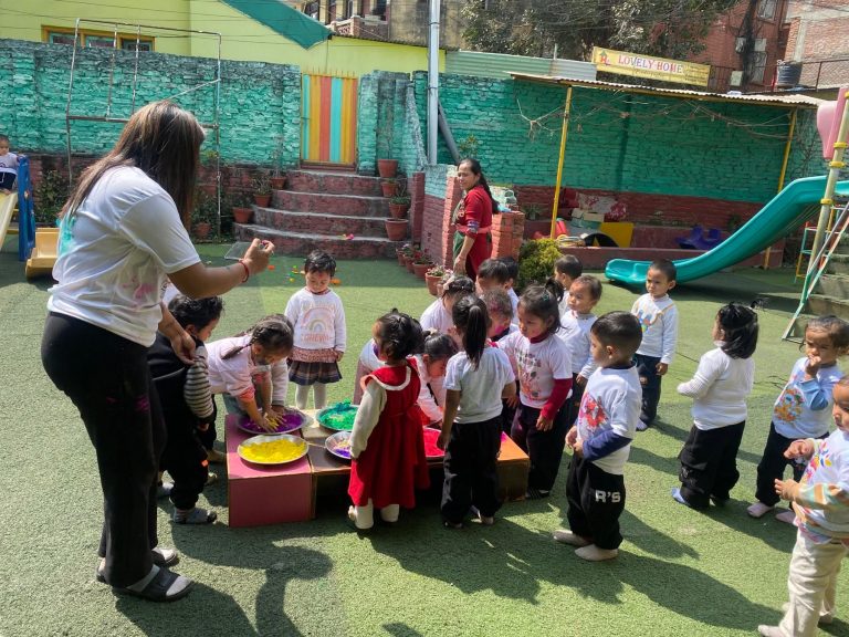 A Lovely Home teacher supervising toddlers playing with Holi colours outside the Jawalakhel branch